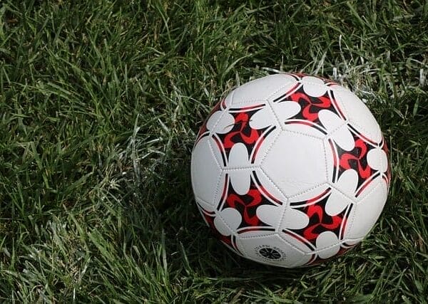 A white and red soccer ball resting on green grass with visible white field lines, a reminder of the solo problem facing teams in coordinating their strategies.