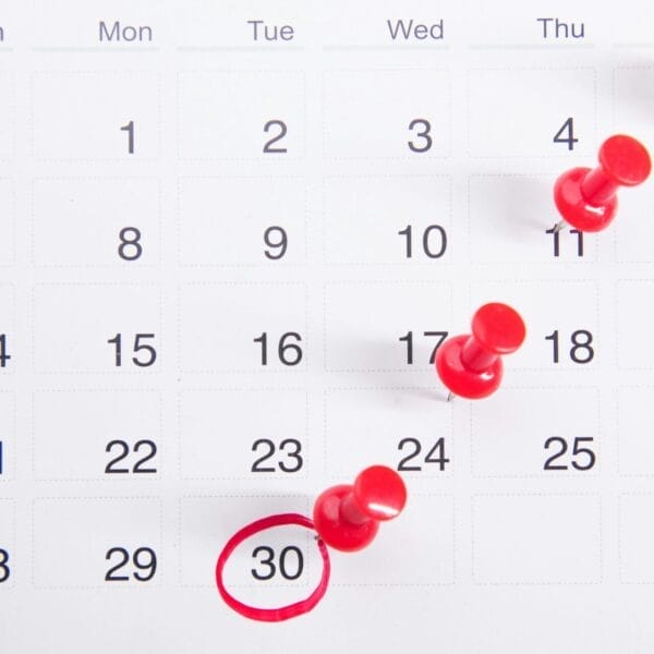 A calendar page with red push pins marking several dates throughout the week, focusing on the 30th circled in red.