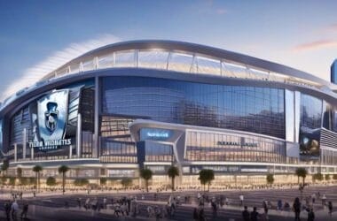 Modern stadium with large screens and distinctive tower nearby, bathed in the warm hues of sunset, surrounded by a bustling cityscape. The air is abuzz with excitement as fans discuss the potential NHL team relocation bringing fresh energy to the town.