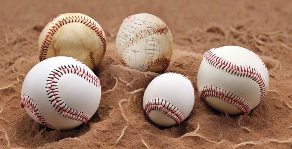 Five baseballs of different sizes and designs rest on a sandy surface, each seeming to narrate its own story through advanced baseball statistics.