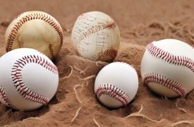 Five baseballs of different sizes and designs rest on a sandy surface, each seeming to narrate its own story through advanced baseball statistics.