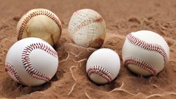Five baseballs of different sizes and designs rest on a sandy surface, each seeming to narrate its own story through advanced baseball statistics.