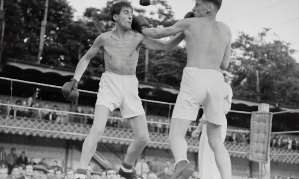 Two boxers face off in the ring, with one landing a punch on the other's face as spectators cheer from the background. The atmosphere buzzes with hot sports takes, fueling the electrifying energy of the match.