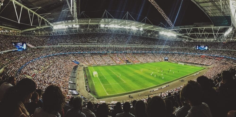 The large stadium buzzes with spectators, enthralled by the soccer match on a well-lit field, as coaches utilize advanced metrics in player evaluation to enhance their strategies.