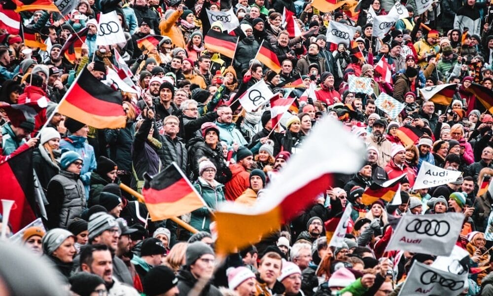 A large crowd, spirited with sports arguments, waves German flags and Audi banners at an outdoor event.