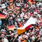 A large crowd, spirited with sports arguments, waves German flags and Audi banners at an outdoor event.