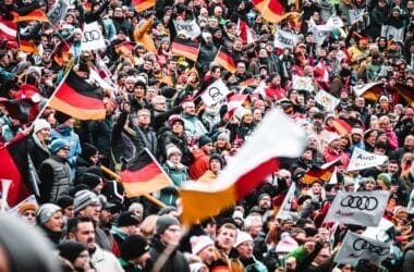 A large crowd, spirited with sports arguments, waves German flags and Audi banners at an outdoor event.