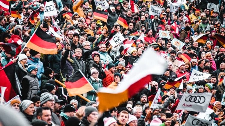A large crowd, spirited with sports arguments, waves German flags and Audi banners at an outdoor event.