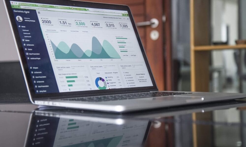 A laptop displaying a data analytics dashboard with various graphs and charts sits on a reflective desk surface, offering insights akin to the evolving statistics in modern sports.