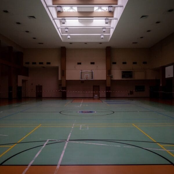 A dimly lit indoor sports hall subtly highlights the basketball hoop and court lines, inviting players to explore the subjectivity in basketball, where every angle can shift perception.