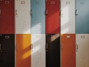 The colorful lockers, arranged in a 3x4 grid and bathed in sunlight, tell silent sports narratives through their varying shades.