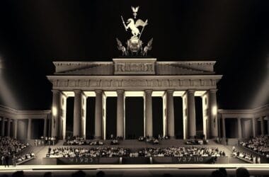 Illuminated Brandenburg Gate at night draws dense crowds, with spotlights highlighting architectural details, much like a gathering for fiery sports opinions under the stars.