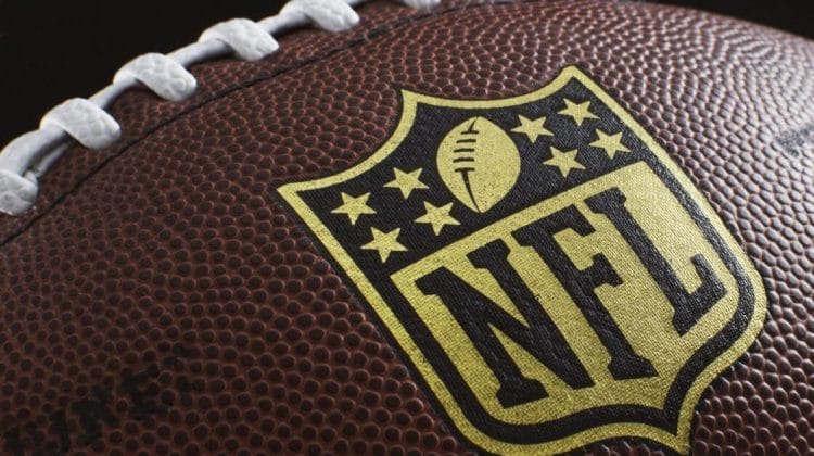 Close-up of an American football showcasing the NFL logo, a symbol of rich NFL traditions. The brown leather surface features white laces and textured pebbling, with the logo prominently centered and highlighted against the football.