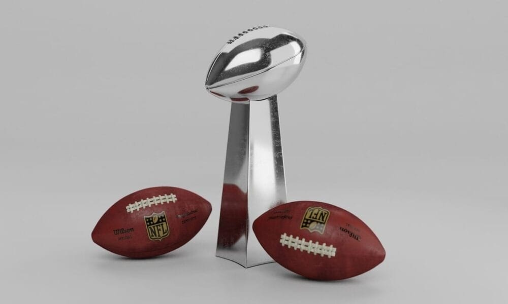 Two footballs flank a shiny silver trophy on a gray background, symbolizing the NFL's tradition of excellence.