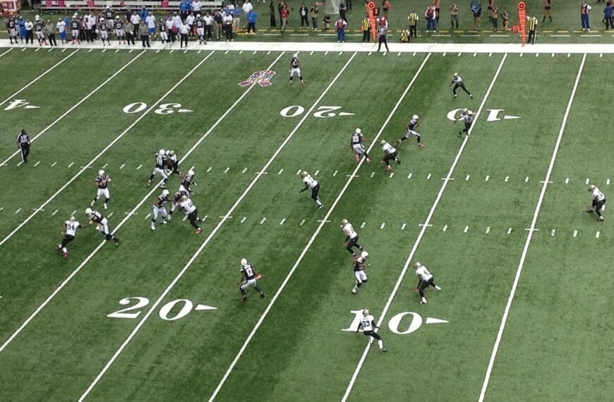 An aerial view captures an American football game in progress on the green field, subtly breaking NFL traditions with innovative strategies that challenge the norm.