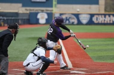 Exploring baseball, a player in a purple helmet and jersey, numbered 12, swings a bat at a pitched ball during the game. A catcher in white gear and an umpire stand behind him on the red and green field.