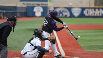 Exploring baseball, a player in a purple helmet and jersey, numbered 12, swings a bat at a pitched ball during the game. A catcher in white gear and an umpire stand behind him on the red and green field.