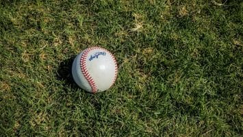 A baseball rests on a grassy field, casting a small shadow, reminiscent of the nuanced precision found in advanced baseball stats.