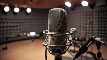 A professional microphone in a recording studio with soundproof padded walls and overhead lights, perfect for capturing sports opinion pieces. Other recording equipment is visible in the blurred background, creating an ideal atmosphere for lively discussions.
