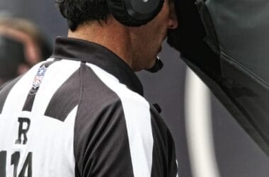 Referee in black and white striped shirt meticulously reviewing a play on a screen during an NFL sporting event, honoring time-honored traditions.