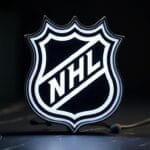 The image shows the official NHL logo, a black and white shield with "NHL" in bold, diagonal letters. The glowing effect on the dark background symbolizes the Evolution of Hockey through time.