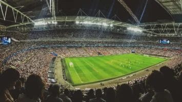 A panoramic view of a packed football stadium reveals thousands of fans, some known as ultras—dedicated supporters whose passion defines football culture. Electronic screens shine while the lively atmosphere fills every seat under a brightly lit roof.