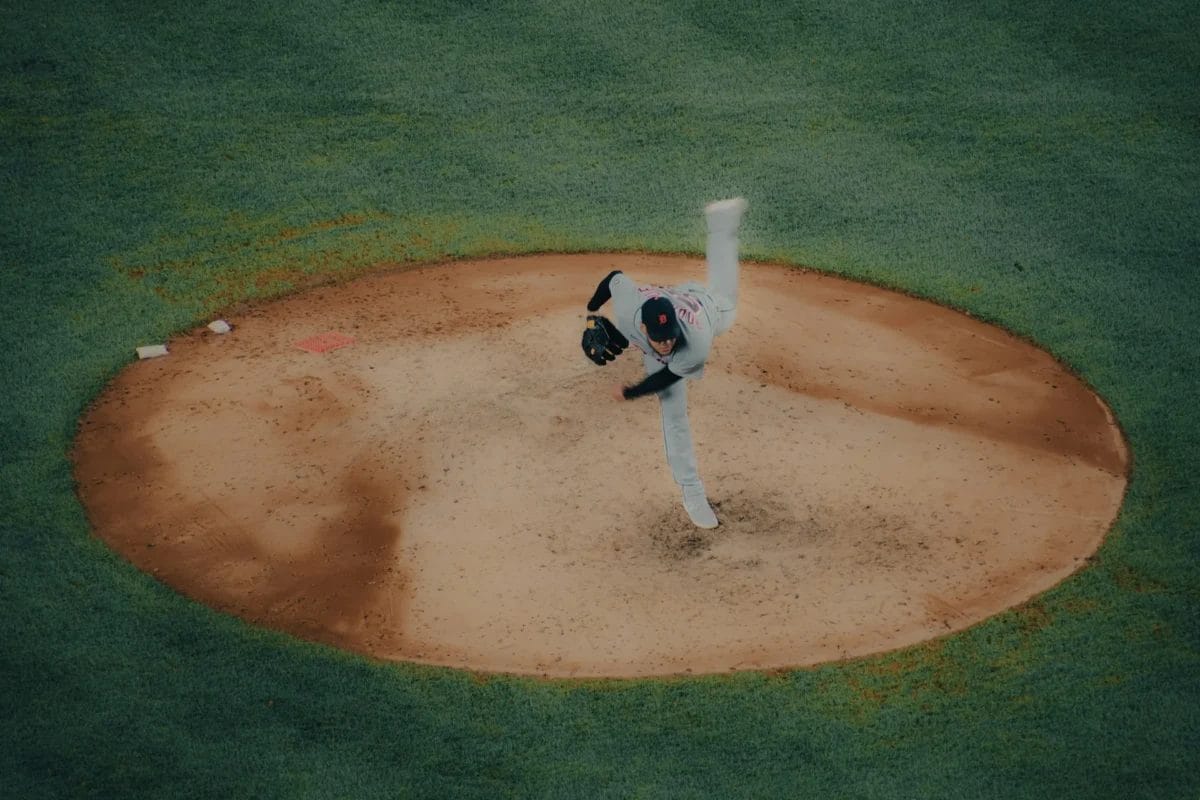 A baseball pitcher in a white uniform is captured mid-pitch atop a brown dirt mound, surrounded by green grass—a striking display of athleticism in the modern baseball era. His right leg is high and his arm extended, highlighting the game's dynamic motion.